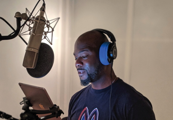 Man recording vocals with microphone and headphones in studio.