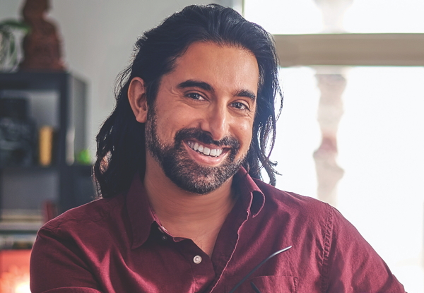 Smiling man with long hair in a red shirt, indoor setting.