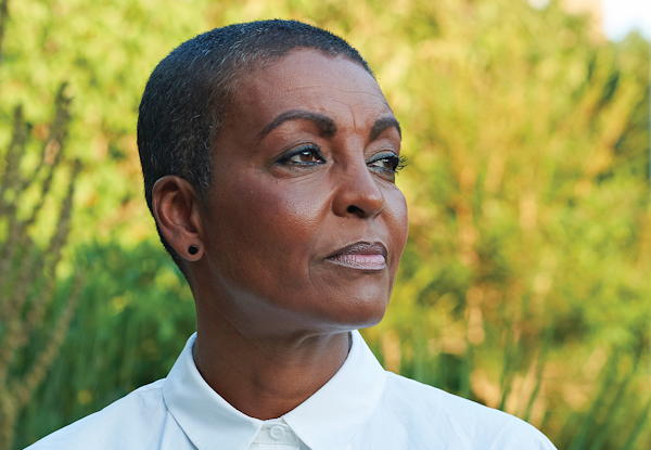 Mature Black woman with short hair, gazing off, wearing a white shirt, nature background.
