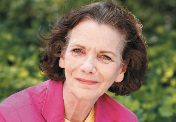 Senior woman smiling outdoors in pink jacket.