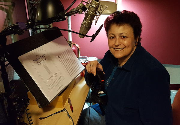 Woman smiling in a radio studio with a microphone and script.