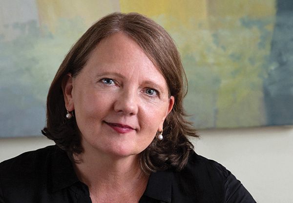 Woman with brown hair and earrings, sitting in front of a pastel artwork.