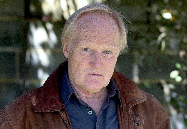 Elderly man with a serious expression wearing a brown leather jacket.