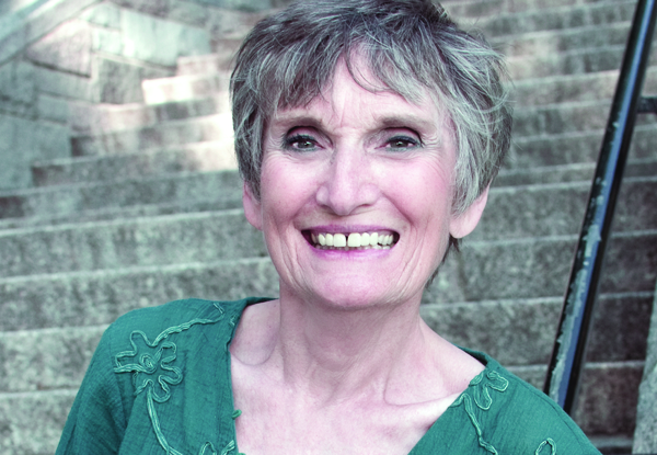 Smiling elderly woman in a green blouse sitting on stone steps.