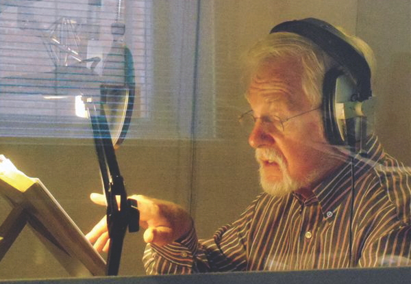 Elderly man with headphones using a microphone in a studio.
