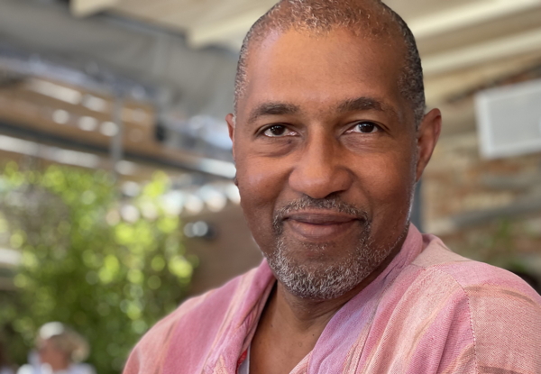 Smiling middle-aged man in a pink shirt at an outdoor café.