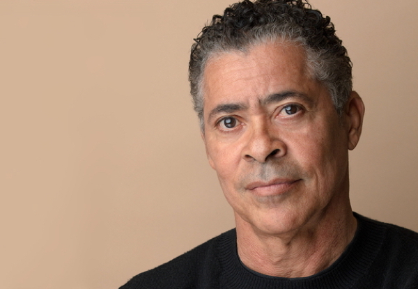 Middle-aged man with gray hair wearing a black sweater against a beige background.