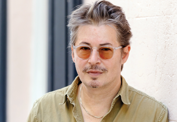 Man with grey hair wearing sunglasses and a khaki shirt.