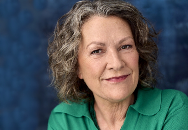 Portrait of a smiling elderly woman with curly gray hair wearing a green blouse.