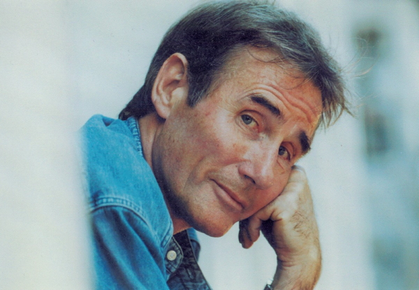 Middle-aged man in denim shirt resting his head on hand, looking thoughtful.