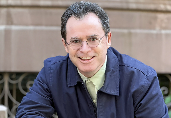 Man with glasses smiling at the camera, wearing a blue jacket.