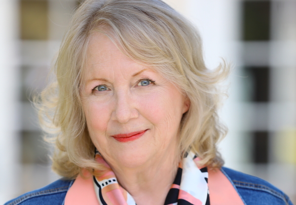 Portrait of a smiling elderly woman with blond hair wearing a scarf and denim jacket.