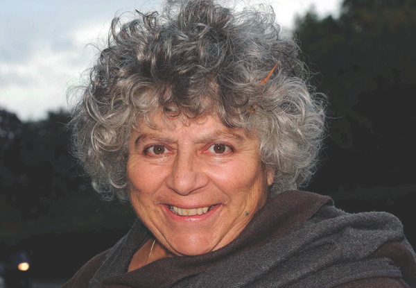 Elderly woman with curly gray hair smiling, wearing a gray shawl.