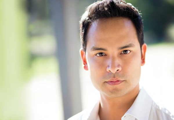 Close-up portrait of a man with a serious expression, outdoors in daylight.