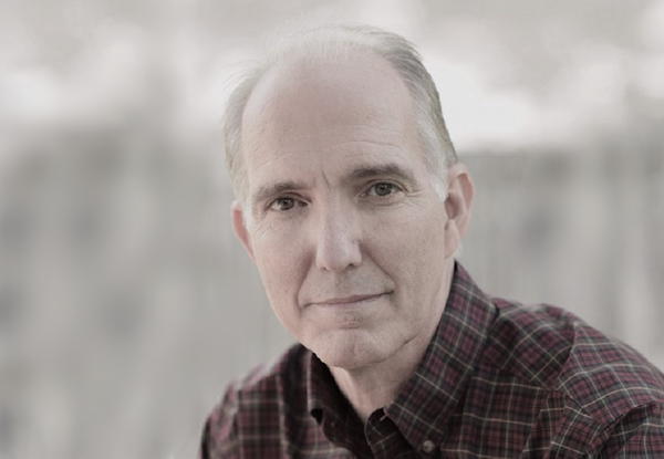 Portrait of an older man in a plaid shirt, gently smiling.