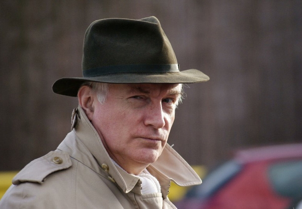 Elderly man in a hat and coat, looking seriously at the camera.