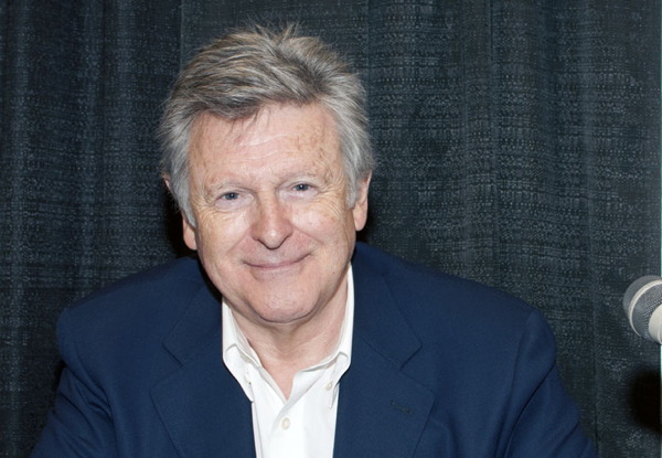 Smiling older man in blue blazer and white shirt at a microphone.