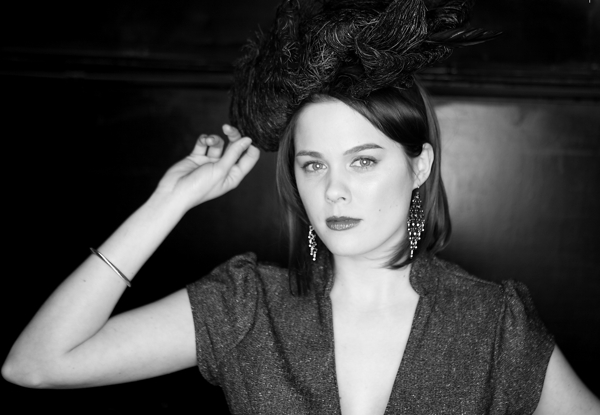 Woman with dramatic feathered hat posing in a black and white photo.