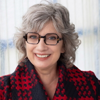 Portrait of a smiling woman with gray hair, glasses, and a red and black scarf.