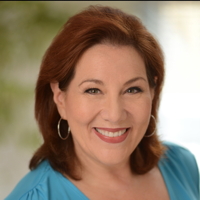 Smiling woman with red hair in a blue blouse against a blurred background.