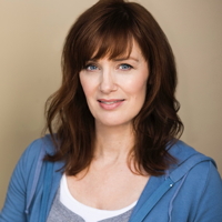 Woman with brown hair, wearing blue cardigan and white top, smiling.