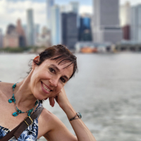 Woman smiling by a river with city skyline in background.