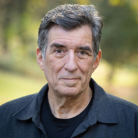 Elderly man with gray hair in a black jacket outdoors.