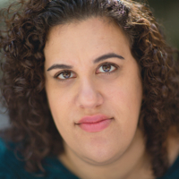 Portrait of a woman with curly hair wearing a blue shirt.