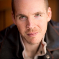 Close-up of a smiling man with short hair in a leather jacket.