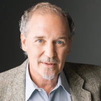 Portrait of an older man smiling, wearing a tweed jacket.