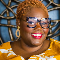 Smiling woman with glasses against a geometric background.