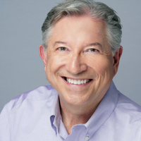 Portrait of a smiling older man with gray hair, wearing a light purple shirt.