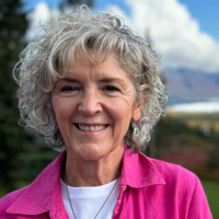 "Senior woman smiling outdoors with a scenic mountain backdrop."